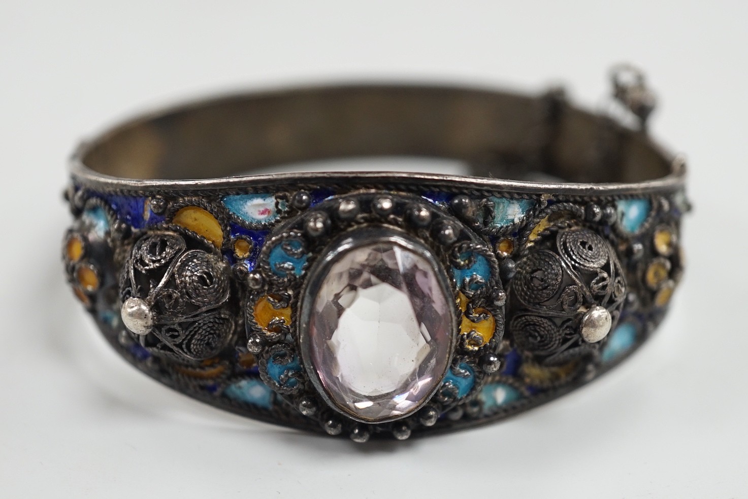An early to mid 20th century continental white metal polychrome enamel and foil backed oval cut rock crystal set hinged bangle, interior diameter approximately 62mm.